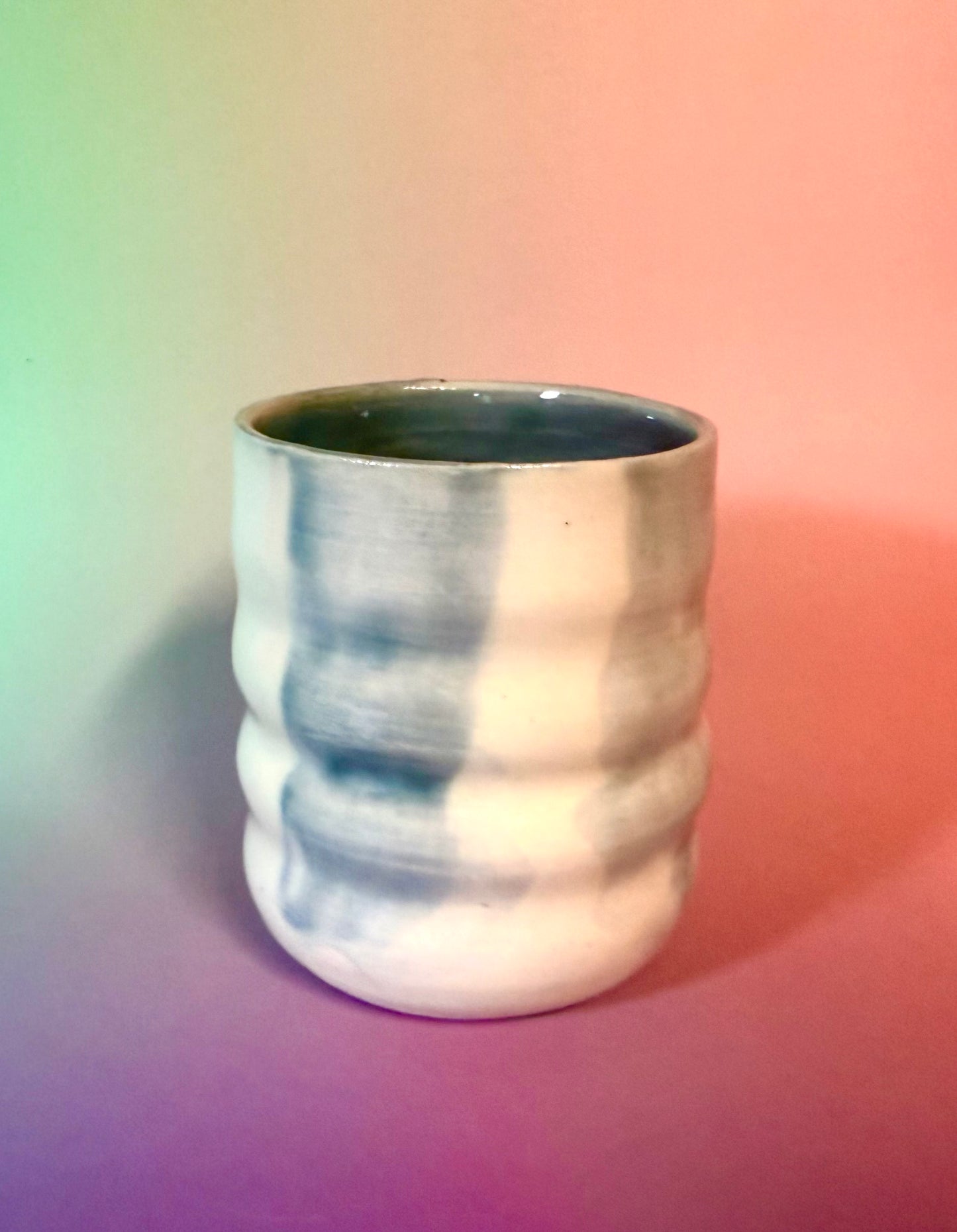 a small porcelain cup with a wave texture. Glazed with 4 watercolor-style blue-gray stripes, and clear glaze exposing the white of the porcelain.